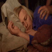 a woman is sleeping on a bed with a man holding her arm