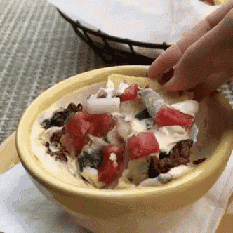 a person is dipping a tortilla chip into a bowl of food .