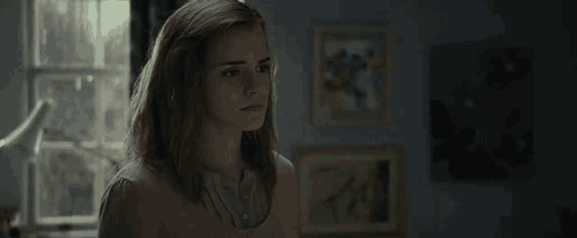 a young woman is standing in front of a window in a room with paintings on the wall .