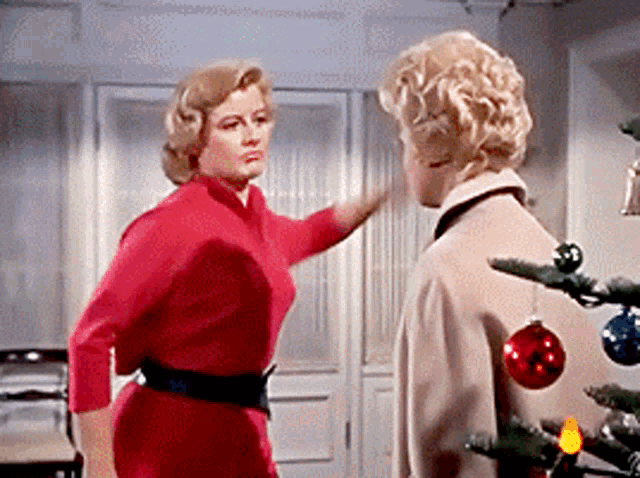 two women are standing next to a christmas tree and talking