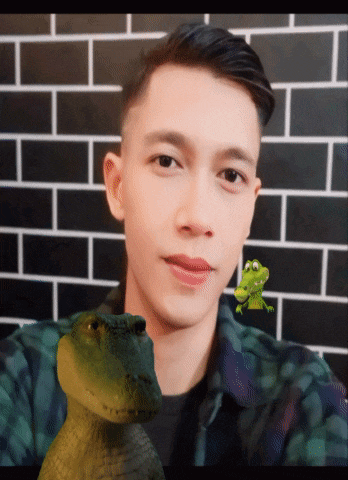 a man is holding a toy crocodile in front of a black brick wall