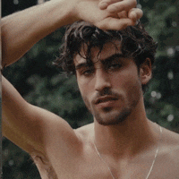 a shirtless man with a beard holds his hand over his face