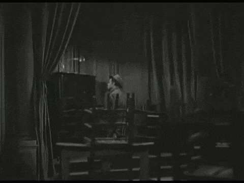 a black and white photo of a man in a hat behind a curtain