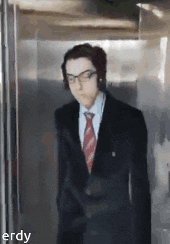 a man in a suit and tie is walking in an elevator with the word erdy below him