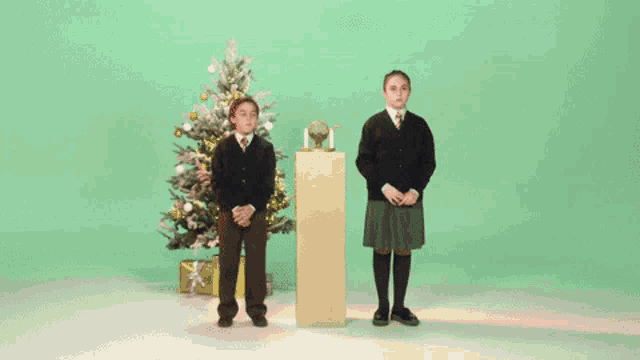 two children are playing with a lottery machine with a christmas tree in the background