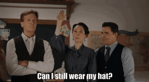 two men and a woman are standing in front of a blackboard with the words can i still wear my hat written on it