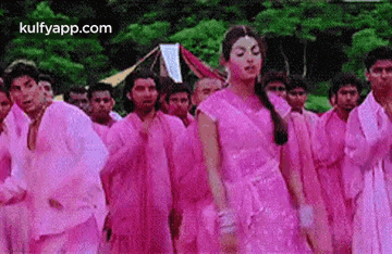 a woman in a pink dress is dancing in front of a group of people in pink clothes .