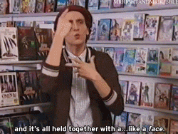 a man standing in front of a shelf of dvds says " and it 's all held together with a like a face "