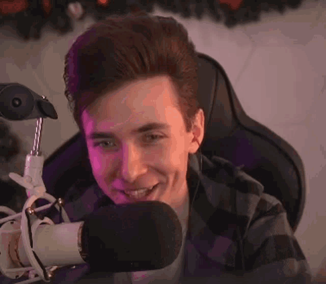 a young man is sitting in a chair in front of a microphone and making a surprised face .