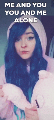 a girl with blue hair is wearing a pink hoodie and holding a stuffed animal