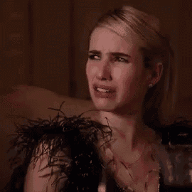 a woman in a black dress with feathers on the sleeves is crying while holding a glass of wine .