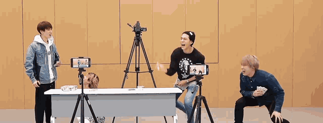 a group of young men are standing around a table with a tripod and camera .