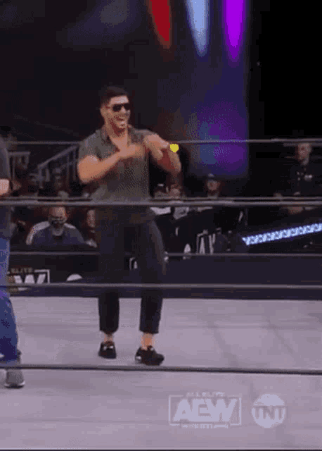 a man is dancing in a wrestling ring while wearing sunglasses and a green shirt .