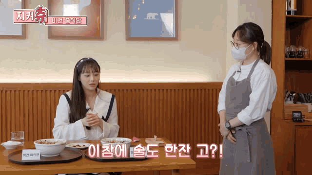 a woman wearing a mask stands next to a woman sitting at a table