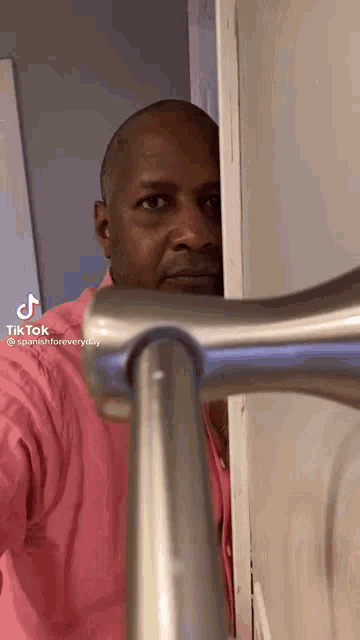 a man in a pink shirt is peeking out from behind a railing and holding a faucet .