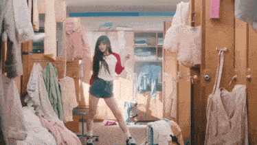 a woman is dancing in a messy room filled with clothes .