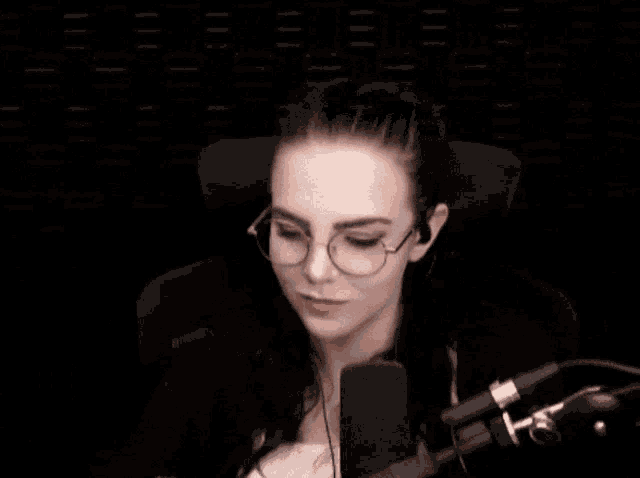 a woman wearing glasses is sitting in front of a microphone and covering her mouth with her hand
