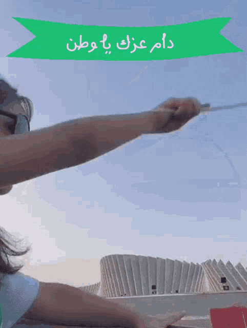 a green banner with arabic writing on it is above a person holding a flag