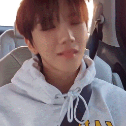 a young man is sitting in the back seat of a car wearing a hoodie and making a funny face .