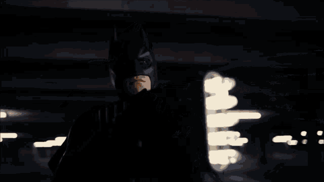a man in a batman costume is riding a bike in a dark parking garage