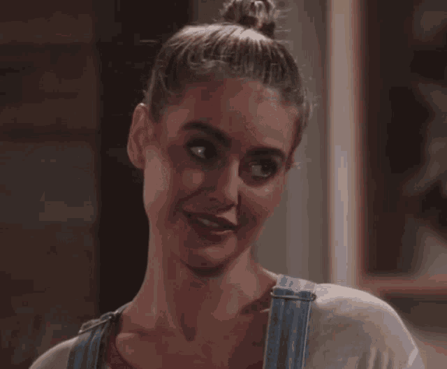 a woman with her hair in a bun and overalls smiles
