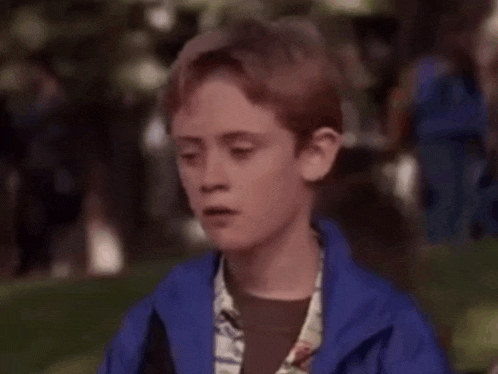 a young boy with red hair is wearing a blue jacket and looking at a woman .