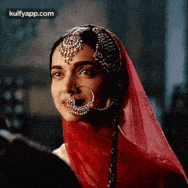 a woman wearing a red veil and a nose ring is looking at a man .