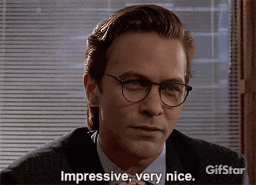 a man with glasses says " impressive very nice " in front of a window