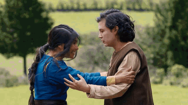 a man and a woman are hugging in a field with trees in the background