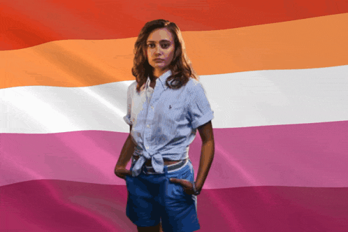 a woman with her hands in her pockets stands in front of a pink and orange flag