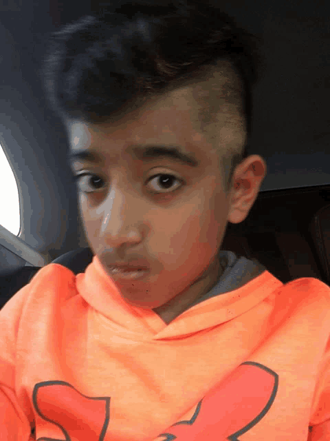 a young boy wearing an orange under armour hoodie