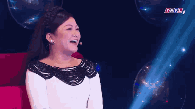a woman in a white dress is laughing in front of a microphone with the letters thvl in the corner