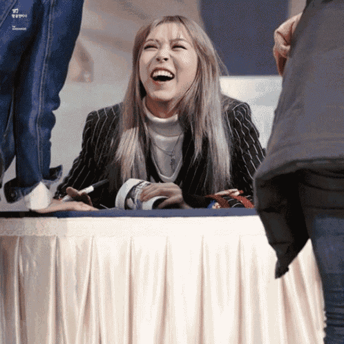 a woman laughs while sitting at a table with a white curtain