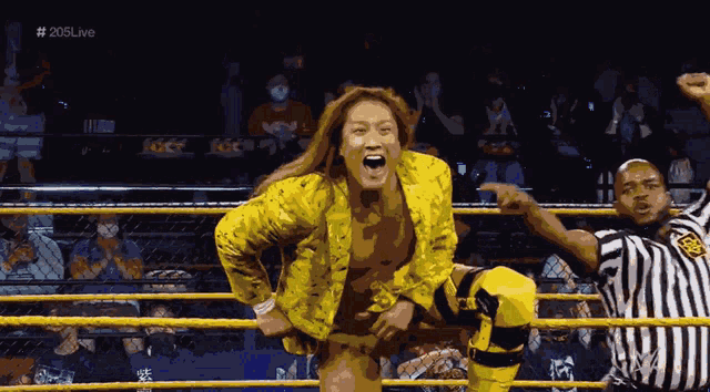 a woman in a yellow jacket stands in a wrestling ring next to a referee with # 205live on the screen