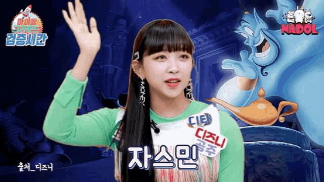 a girl in a green shirt is waving her hand in front of a cartoon of a genie