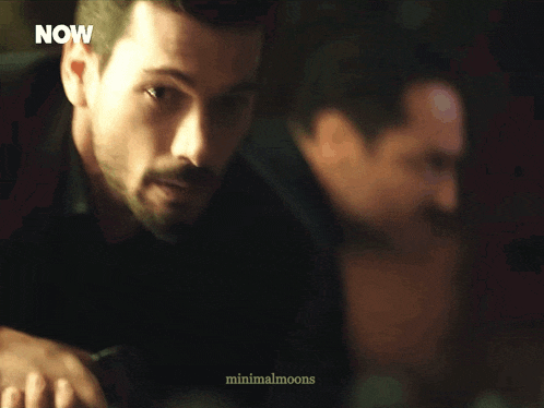 a man with a beard is standing in front of a now advertisement