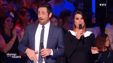 a man in a suit and tie is standing next to a woman in a black dress holding a microphone .