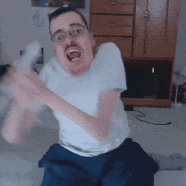a man in a white shirt and blue shorts is sitting on a bed with his mouth open