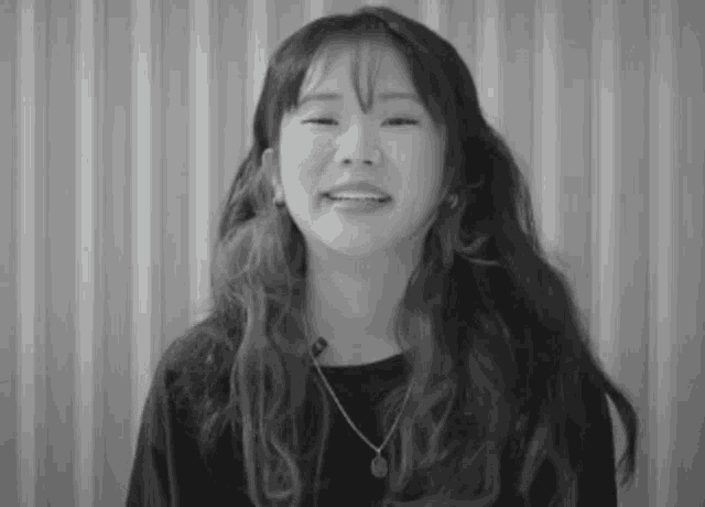 a black and white photo of a woman with long hair wearing a necklace .