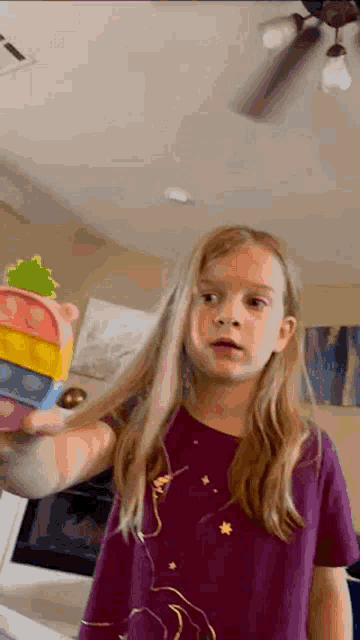 a little girl is standing in a living room holding a toy .