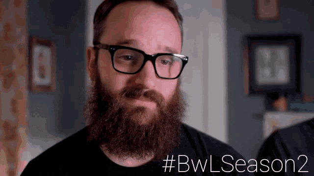 a man with glasses and a beard is looking at himself in a mirror ..