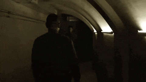 a man is walking through a dark tunnel with a light on the wall