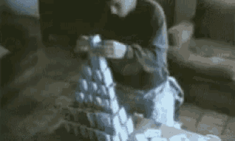 a man is kneeling down and making a castle out of cans of soda .