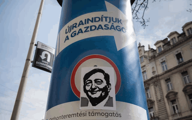 a blue pole has a sticker of a man on it that says ' urainditjuk a gazdasago '