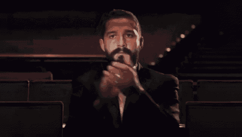 a man in a tuxedo and bow tie is sitting in a theater applauding .