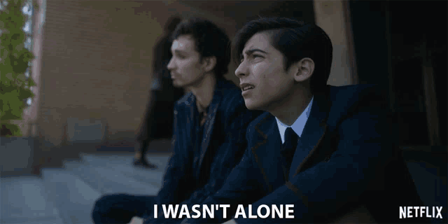 a man in a suit sits next to another man with the words i wasn 't alone below him
