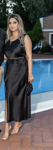 a woman in a black dress stands in front of a swimming pool