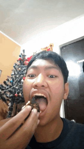 a man with his tongue hanging out eating a piece of food in front of a christmas tree