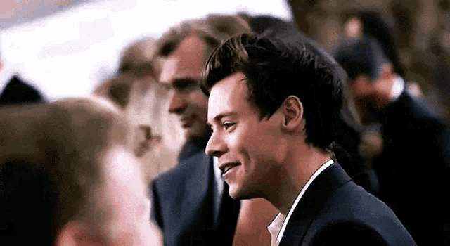 harry styles is smiling while talking to a group of people .