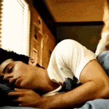 a man in a white shirt is laying on his stomach in bed